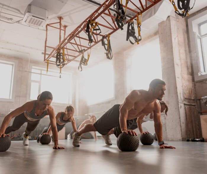 Handsome shirtless muscular male trainer and sporty women using exercise balls while having workout at industrial gym