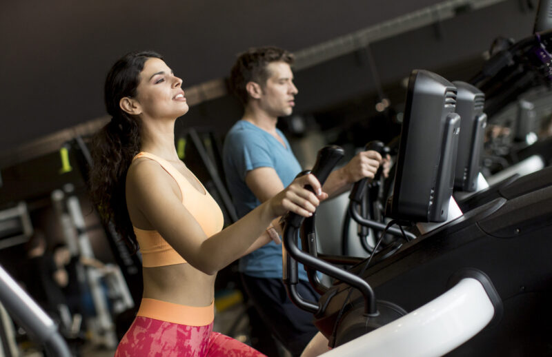 Close up view at woman and man on elliptical stepper trainer exercising in gym