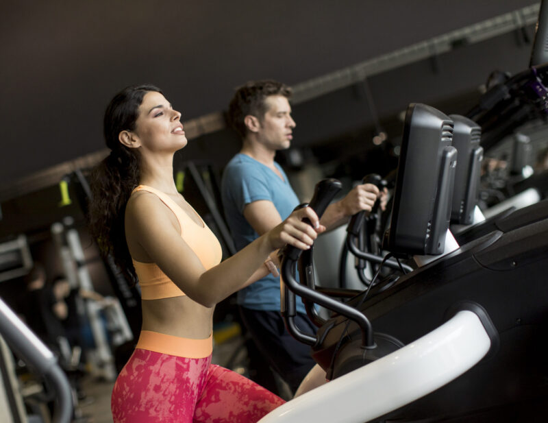 Young woman and man on elliptical stepper trainer exercising in Close up view at woman and man on elliptical stepper trainer exercising in gym